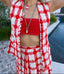 Person wearing a red and white checkered outfit with a necklace by a poolside.